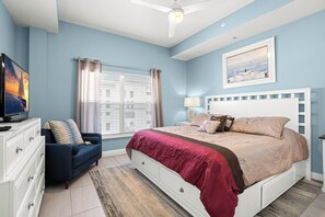 A bedroom with a bed, a dresser, a television, a window with curtains, and a painting on the wall.