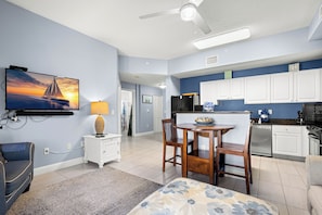 A modern kitchen with white cabinets, a dining area with a table and chairs, a TV mounted on the wall, and a ceiling fan.