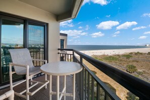 A balcony with a view of the beach, a chair, and a small table. - 🌅 Prime View Condo — Gulf Strand Resort, St. Pete Beach (St Pete Beach)