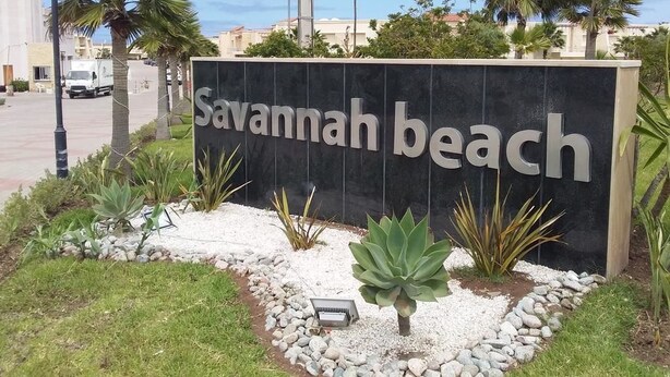 A sign for Savannah Beach with a landscaped area featuring rocks and plants. - Savannah Beach (Sidi Rahal)