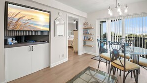 A modern kitchen with white cabinets, a dining area with a glass table and metal chairs, and a large window with a view. - 🌴 Gulf View Condo — Gulf Strand Resort, St. Pete Beach (St Pete Beach)