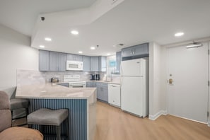 Une cuisine moderne avec des meubles gris, un réfrigérateur blanc, un four à micro-ondes et un îlot central intégré avec des tabourets de bar.