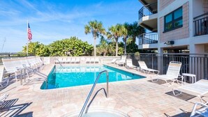 A swimming pool with lounge chairs and an American flag, surrounded by palm trees and a multi-story building. - 🌴 Gulf View Condo — Gulf Strand Resort, St. Pete Beach (St Pete Beach)