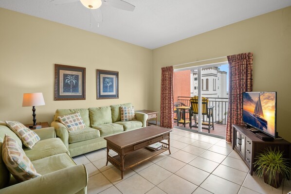 A living room with a sofa, coffee table, TV, and balcony with curtains.