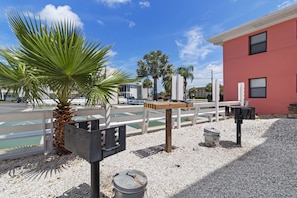 A parking area with a palm tree, a red building, and a white fence.