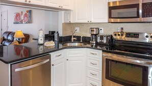 A modern kitchen with white cabinetry, stainless steel appliances, and a black countertop.