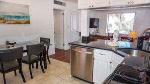A modern kitchen with a dishwasher, a dining area with chairs, and a painting on the wall.