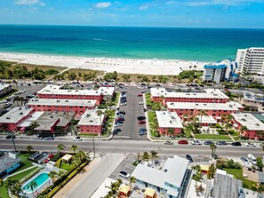 A coastal hotel with multiple red-roofed buildings, a parking lot, and a beach in the background.