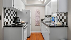 Una cocina compacta con armarios blancos, un salpicadero blanco y negro a cuadros, una isla central y un perchero en la pared.