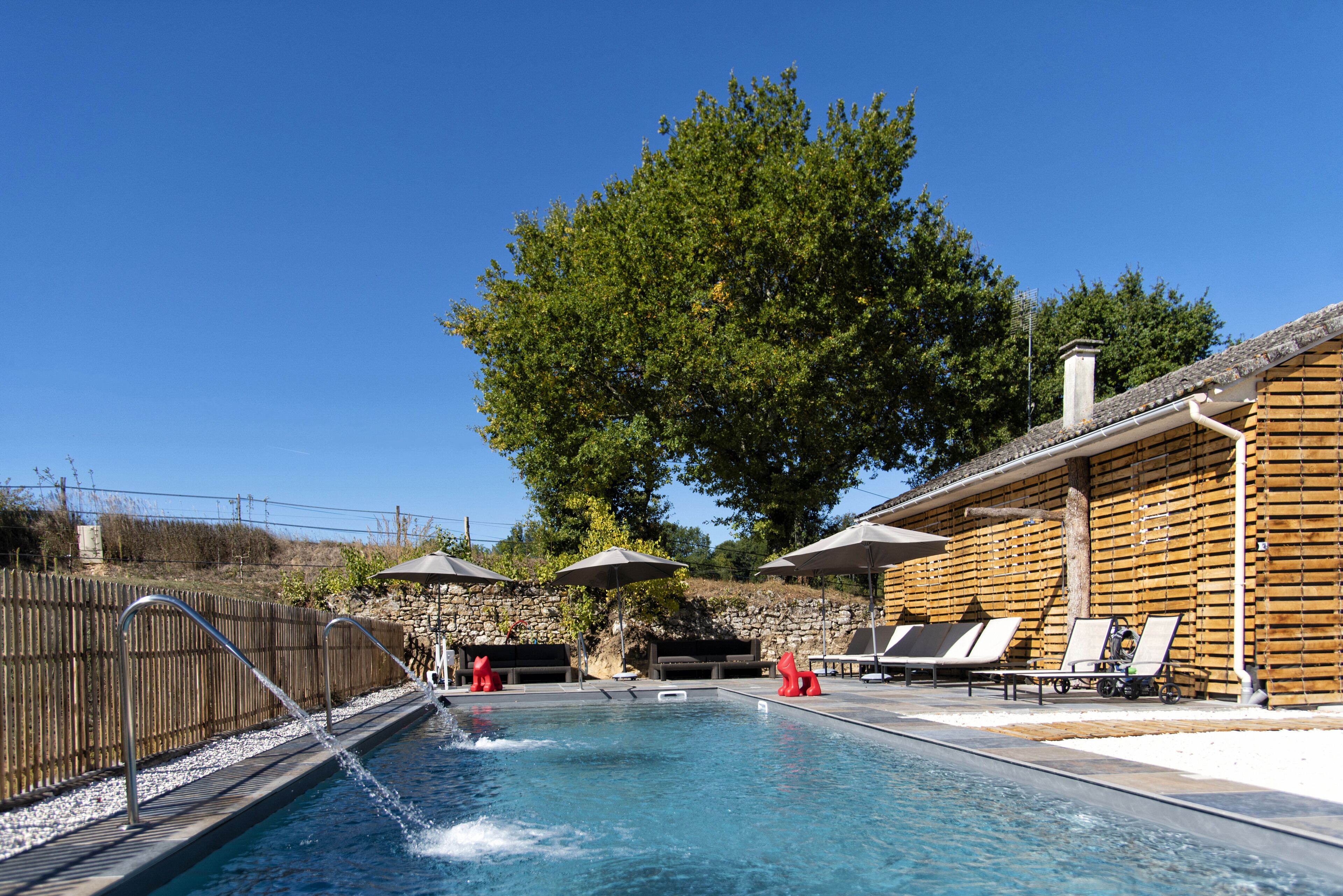 Un área de piscina con sillas de descanso, sombrillas y un edificio de madera.