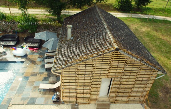 Une cabane en bois avec un toit en tuiles, une piscine et un espace salon extérieur.