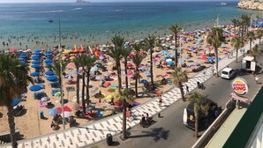 A beach with numerous umbrellas and people, a Burger King sign, and a Benidorm sign.
