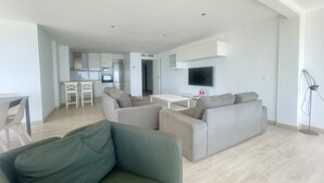 A modern living room with a sofa, a dining table, and a kitchen area in the background.