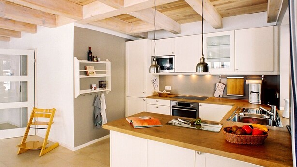 Una cocina moderna con vigas de madera, armarios blancos y una isla central con una cesta de fruta.