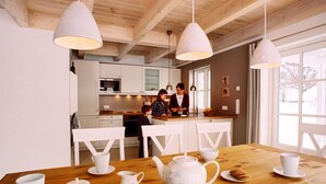 Una cocina moderna con armarios blancos, una mesa de comedor de madera con vajilla blanca y luces colgantes.