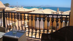 A balcony with a view of the sea, featuring a railing, a wicker chair, and a table with a vase. - SEAHAUS FUERTE in a residential complex directly on the sea. (Corralejo)