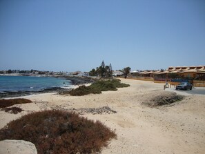 Zona costera con playa arenosa, mar azul cristalino y edificios con techos de tejas rojas.
