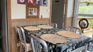 A dining area with a table set for four, surrounded by metal chairs. Above the table, there is a shelf with decorative items and a sign that reads "CAFE". - Cottage in the forest with heated pool from May to October (Buhl)