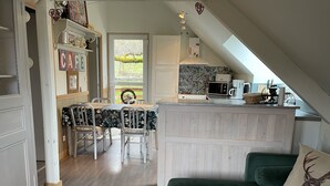 A cozy kitchen with a dining area, a green couch, and a view of the outdoors. - Cottage in the forest with heated pool from May to October (Buhl)