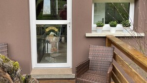 A cozy entrance with a glass door, a wicker chair, and a wooden deck. - Cottage in the forest with heated pool from May to October (Buhl)
