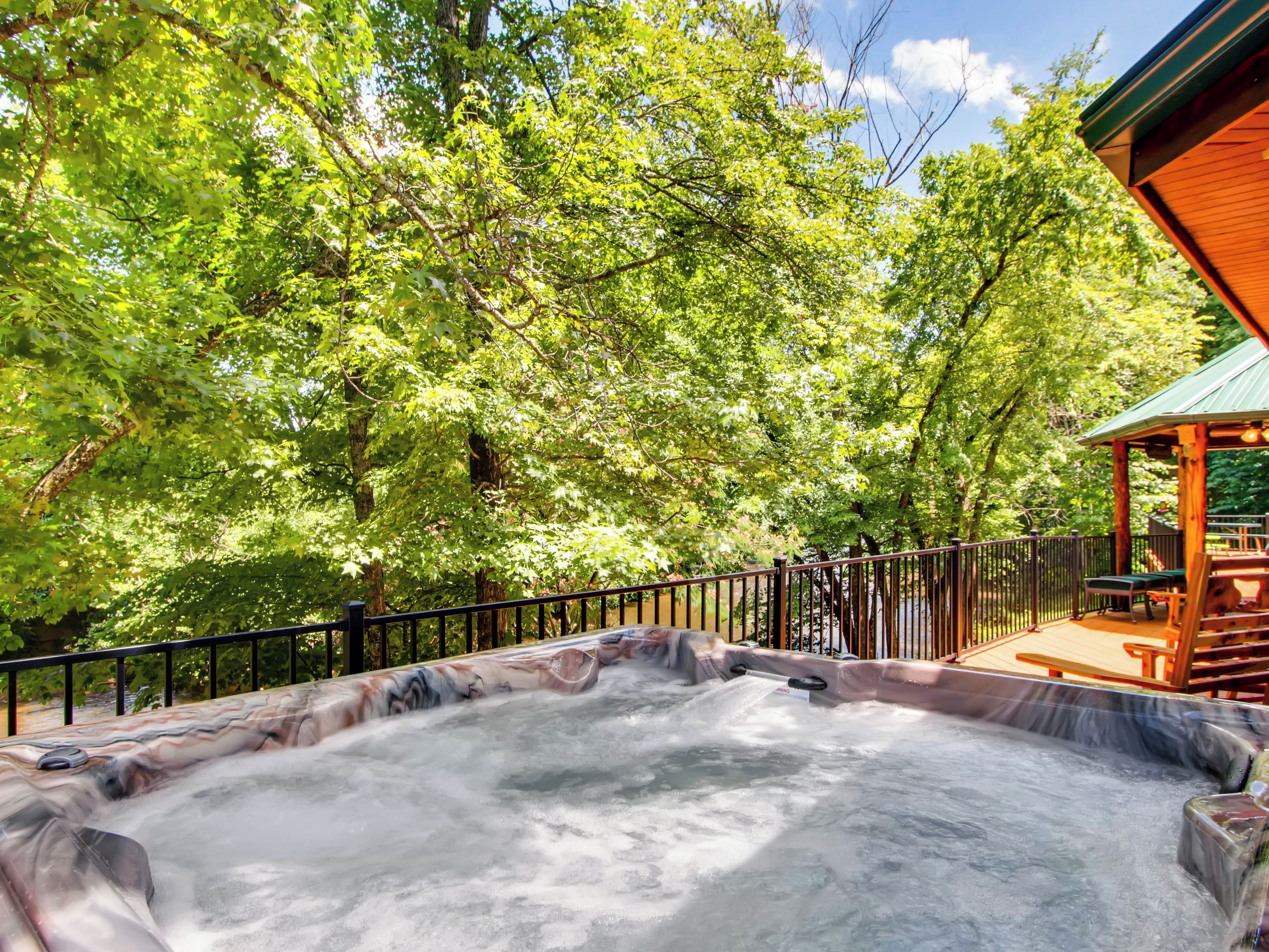 A hot tub surrounded by a wooden deck and a gazebo, with trees in the background.