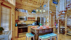 A wooden cabin kitchen with a central island, bar stools, a microwave, stove, refrigerator, and a hanging light fixture.
