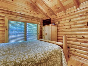 Habitación de cabaña de madera con una cama, un armario de madera y una ventana con persianas.