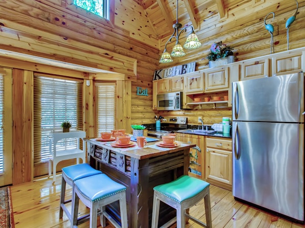A wooden cabin kitchen with a central island, stainless steel appliances, and a dining area with stools.