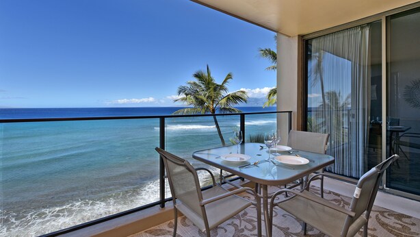 Un balcon avec une table dressée pour deux personnes, donnant sur une plage bordée de palmiers et sur l’océan.