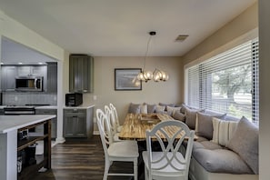 A modern kitchen with grey cabinets, a built-in microwave, and a dining area with a wooden table and white chairs. - Gorgeous townhouse with spectacular golf views in Palmetto Dunes! (Hilton Head Island)