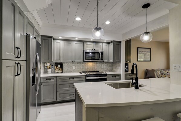 A modern kitchen with grey cabinets, a stainless steel refrigerator, a microwave, and a large island with a sink. - Gorgeous townhouse with spectacular golf views in Palmetto Dunes! (Hilton Head Island)
