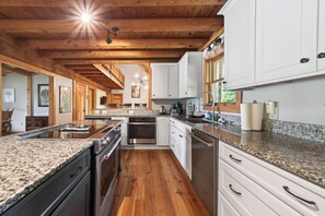 Une cuisine dotée de plans de travail en granit, d’armoires en bois, d’un îlot central et d’un plafond en bois.