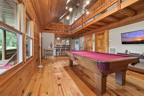 A wooden interior with a pool table, wooden ceiling beams, and a TV on the wall.