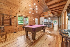 Un interior de madera con mesa de billar, paredes de madera y zona de comedor.