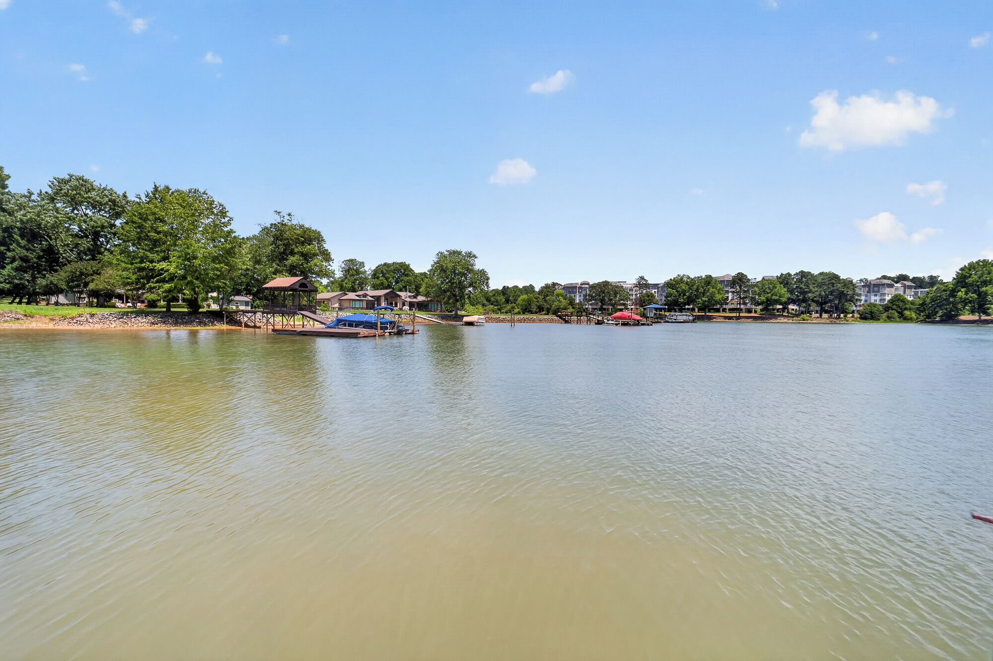 Een rustig meer met een pier, boten en een rij huizen langs de oever.
