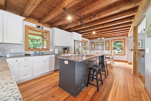 A spacious kitchen with wooden beams, granite countertops, and a central island with stools.