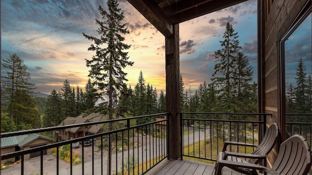 Een houten terras met Adirondack-stoelen met uitzicht op een bebost gebied bij zonsondergang.