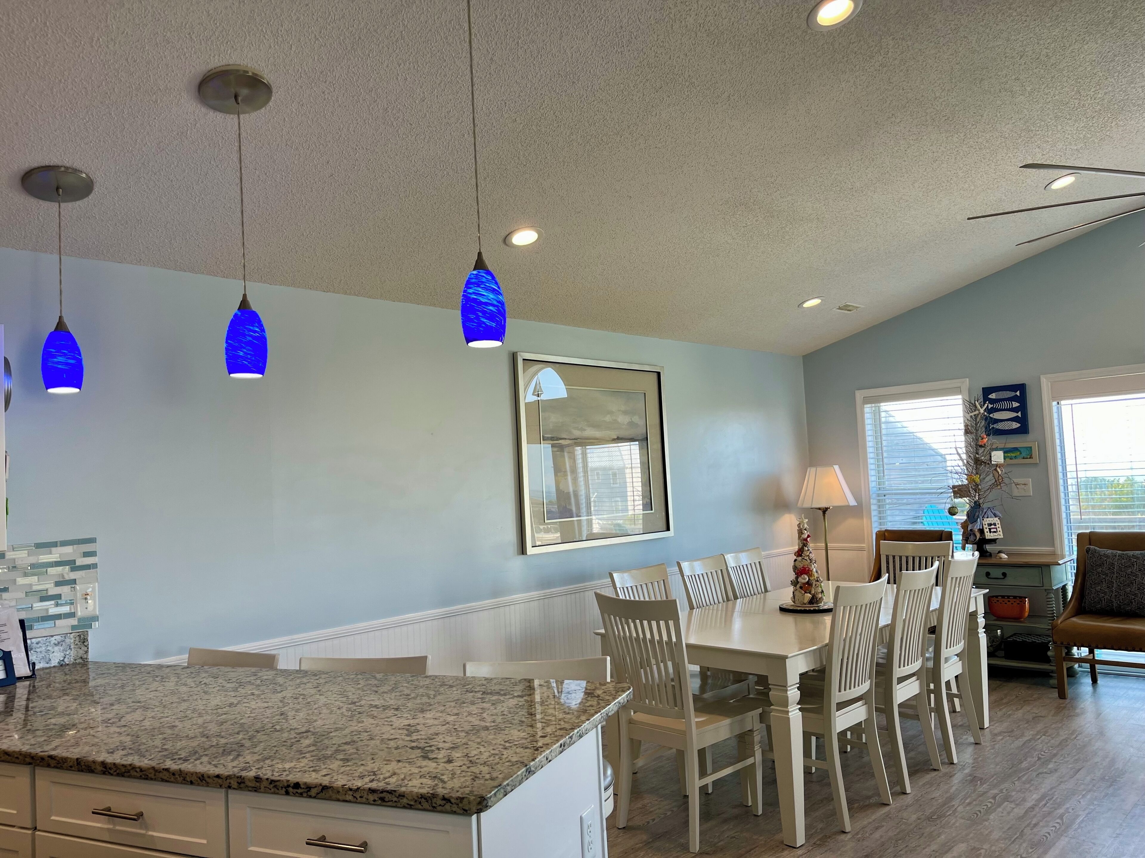 A kitchen with granite countertops, white cabinetry, and blue pendant lights.