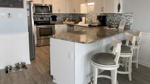 Una cocina moderna con armarios blancos, encimera de granito, electrodomésticos de acero inoxidable y lámparas colgantes azules.
