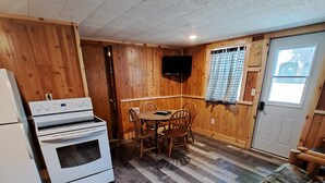 A room with a wooden floor, a bed with a patterned blanket, a dining table with chairs, a television mounted on the wall, and a refrigerator. - Cottage 4 is great for family gatherings, & fishing on Lake Osakis! (Osakis)