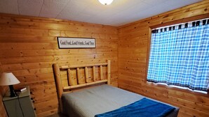 A wooden cabin room with a bed, a nightstand, a lamp, and a window with a plaid curtain. - Cottage 4 is great for family gatherings, & fishing on Lake Osakis! (Osakis)