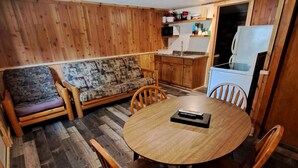 A cozy room with a wooden floor, a round wooden table with chairs, a sofa, and a kitchen area with a refrigerator and microwave. - Cottage 4 is great for family gatherings, & fishing on Lake Osakis! (Osakis)