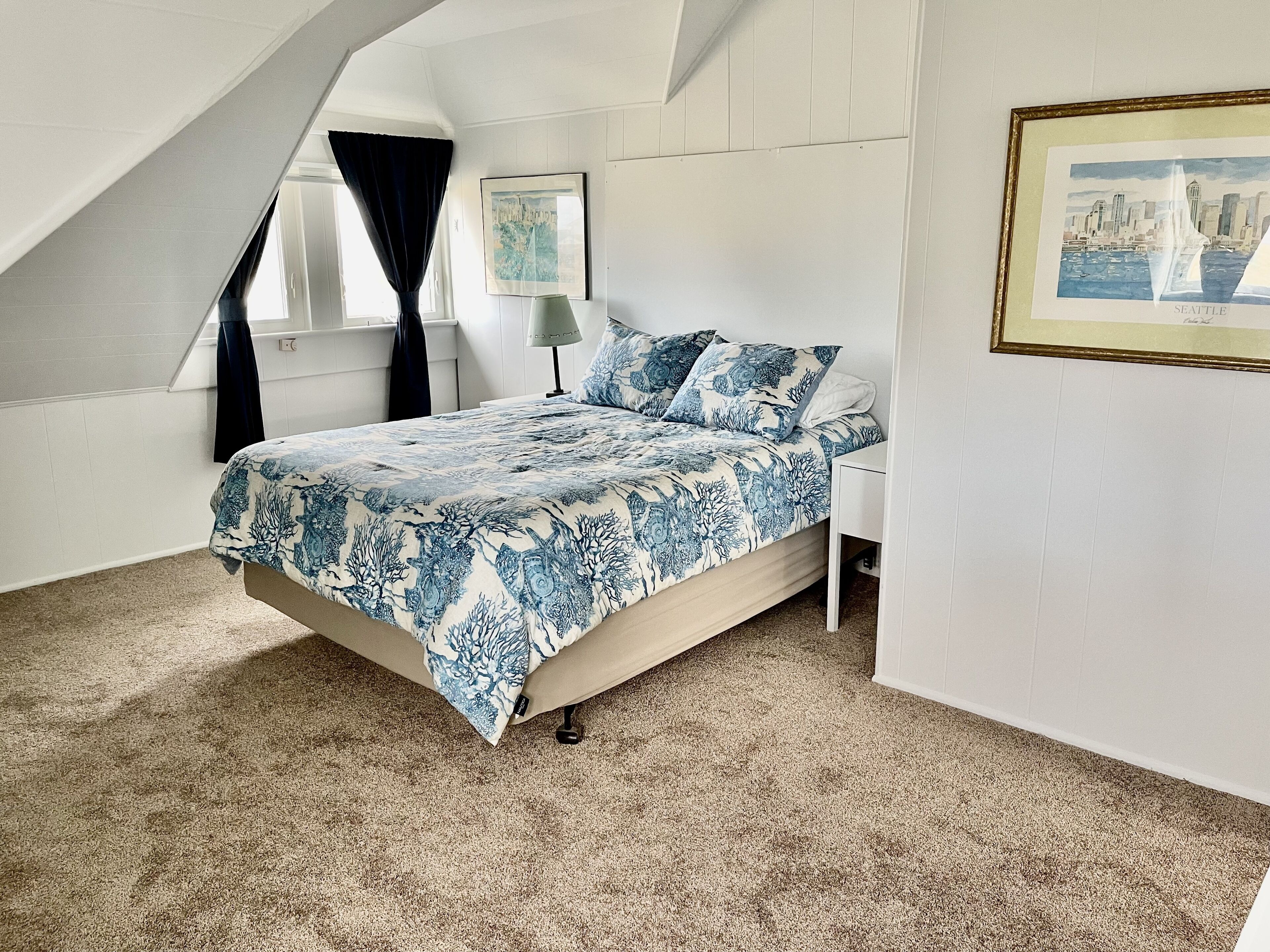A bedroom with a bed, a window with curtains, a lamp, and a framed picture on the wall.