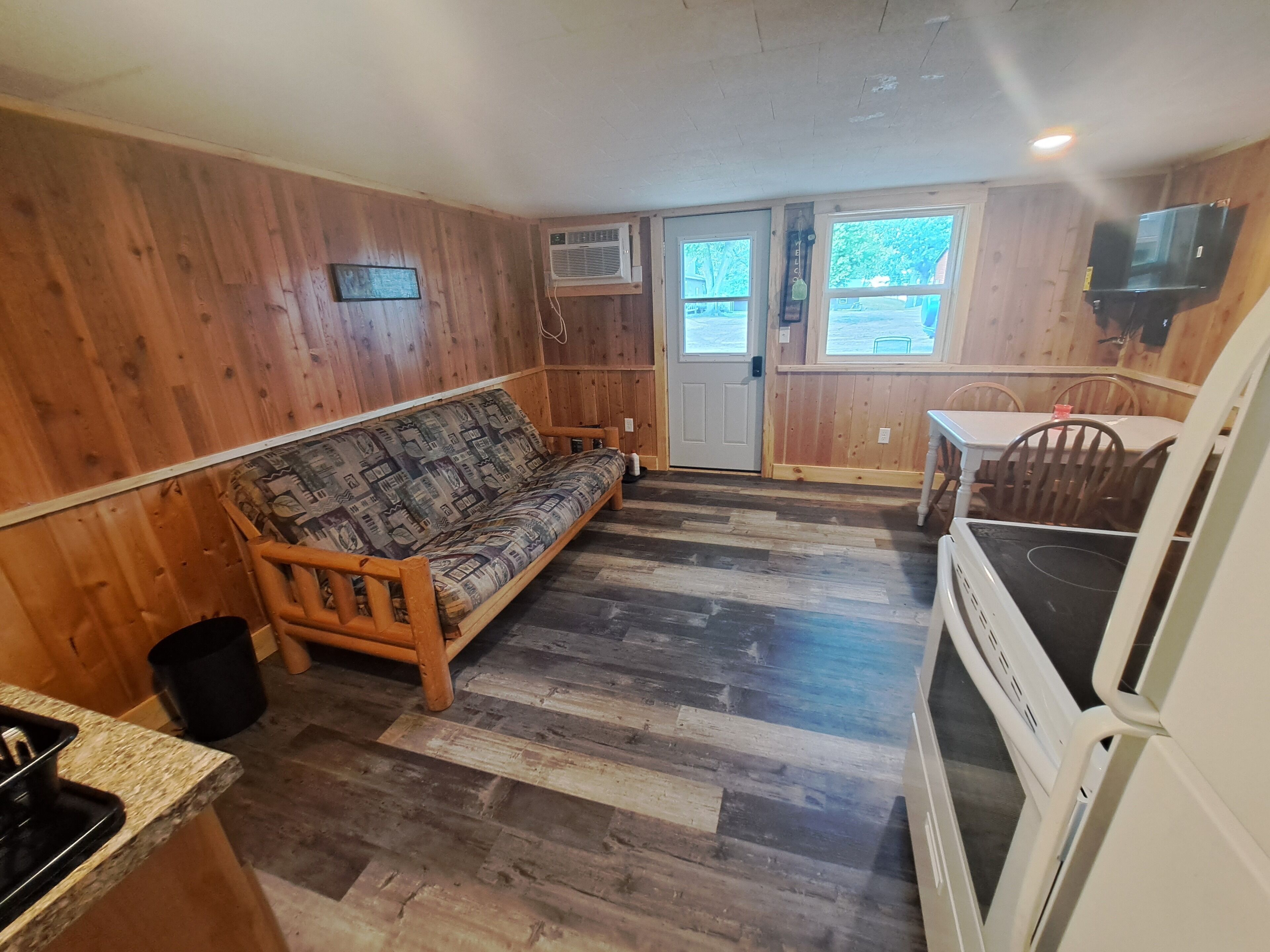 Een knus interieur van een chalet met een bank, houten wanden, een keukenhoek en een eettafel.