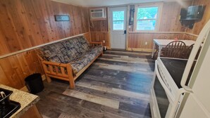 A cozy cabin interior with a sofa, wooden walls, a kitchen area, and a dining table. - Cottage 5 is great for family gatherings, & fishing on Lake Osakis! (Osakis)
