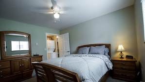 Une chambre à coucher avec un lit, une commode en bois, une table de chevet et un ventilateur de plafond.