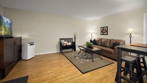 Un salon avec un plancher en bois, un canapé, une table basse, un téléviseur et un réfrigérateur.