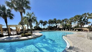A clear swimming pool with a curved edge, surrounded by palm trees and lounge chairs. - Beautiful Sunset paradise with New Golf Cart 4811 (Miramar Beach)
