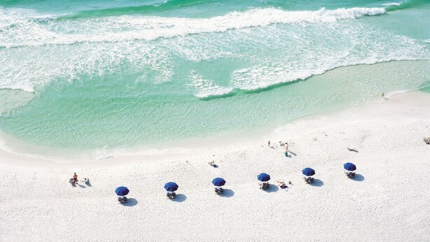 A beach with clear turquoise water and white sand. There are several blue umbrellas and beach chairs. - Beautiful Sunset paradise with New Golf Cart 4811 (Miramar Beach)