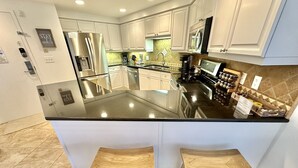 A modern kitchen with white cabinets, a stainless steel refrigerator, a microwave, and a built-in island with stools. - Beautiful Sunset paradise with New Golf Cart 4811 (Miramar Beach)